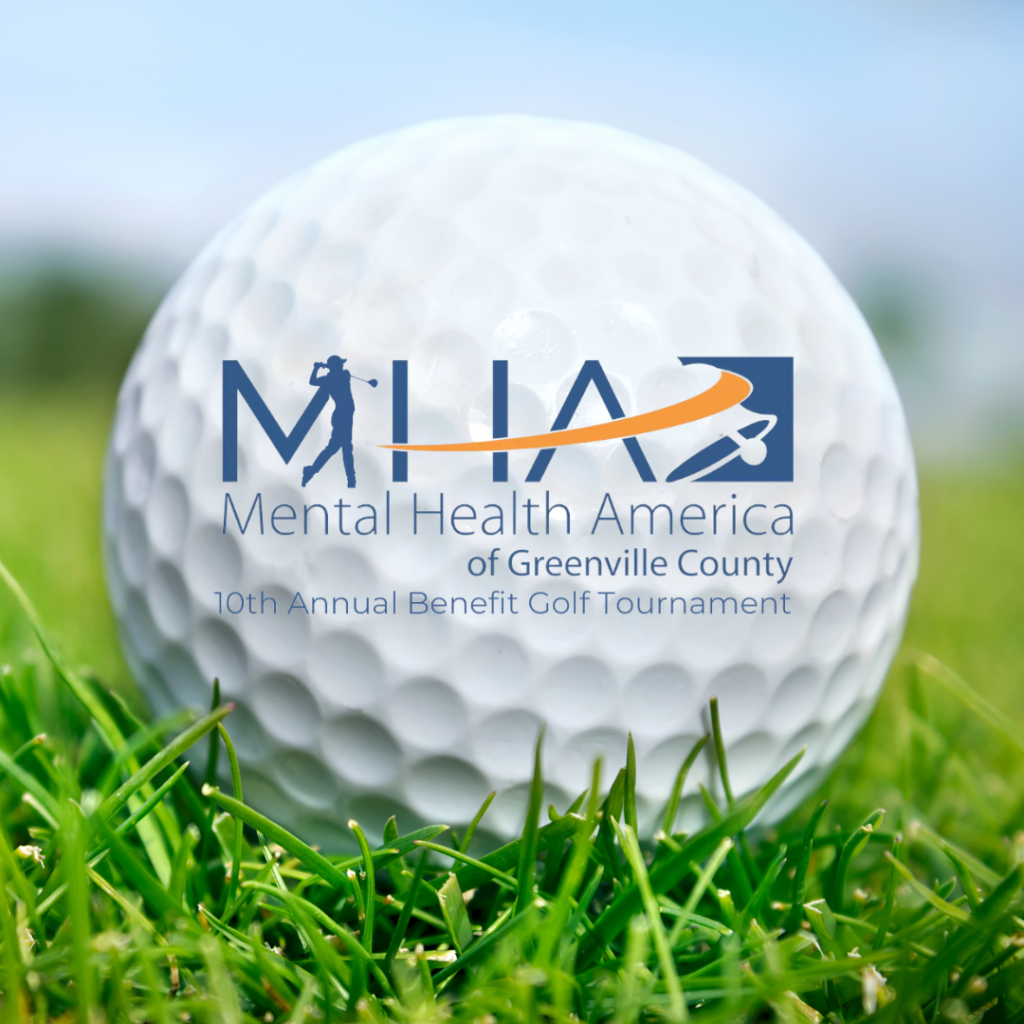 On a field of green grass with blue sky in the background, a golf ball emblazoned with the MHAGC logo.